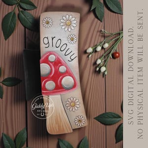 May include: Wooden mushroom-shaped sign with a red cap and white spots, the word "groovy" in a curved font, and daisy accents. The sign is a digital download from Giddy Up's Studio.