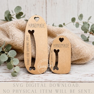 May include: Two light brown, oval-shaped wooden display tags with laser-cut details. Each tag features a heart cutout at the top, a bone-shaped cutout in the center, and the text "HANDMADE" and "THANKS FOR SHOPPING SMALL" engraved on the surface.