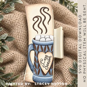 May include: A rectangular hair claw clip featuring a graphic of a blue mug filled with marshmallows and steam. A heart-shaped tag on the mug reads "Cozy Season". Text on the right side states: "SVG DIGITAL DOWNLOAD. NO PHYSICAL ITEM WILL BE SENT."