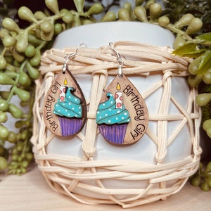 May include: A pair of wooden earrings with a teal cupcake design and the text "Birthday Girl".