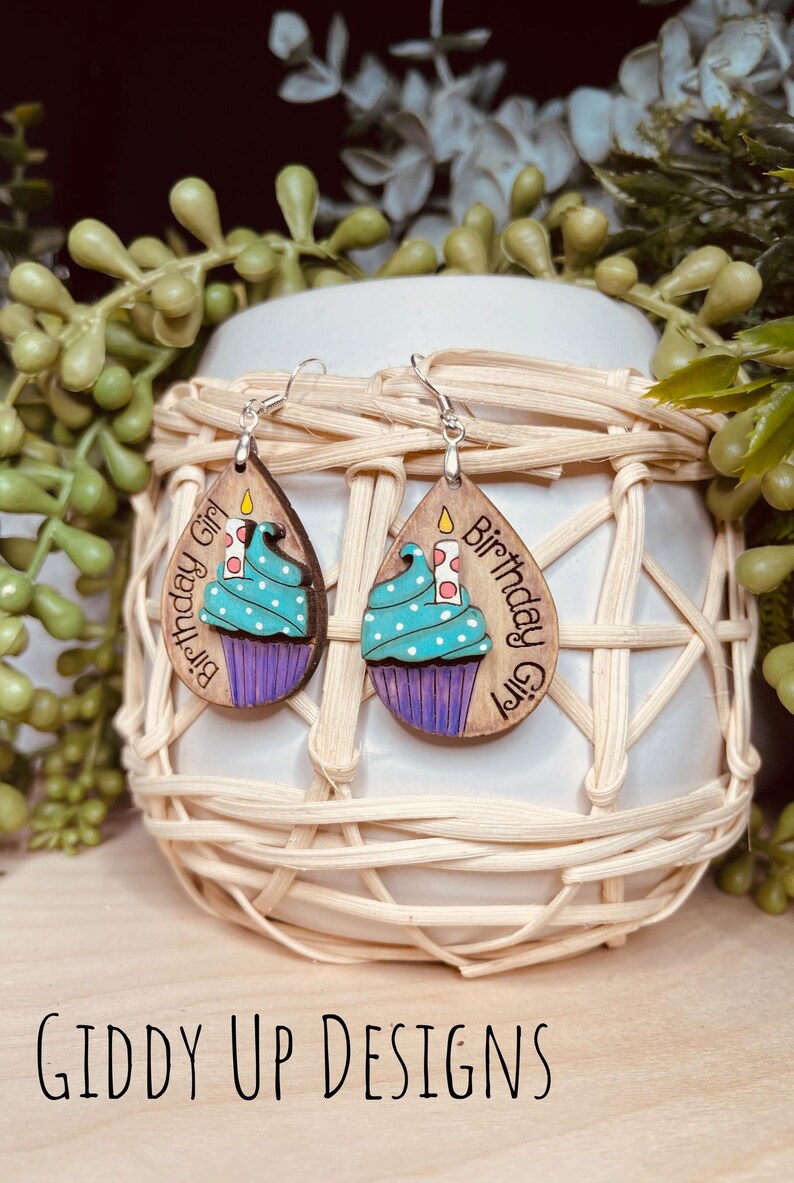 May include: A pair of wooden earrings with a teal cupcake design and the text "Birthday Girl".