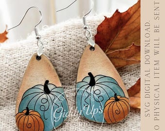 Puede incluir: Pendientes de madera en forma de lágrima con una calabaza azul claro con detalles negros y una calabaza naranja. Los pendientes tienen ganchos plateados. El fondo es de color beige claro.
