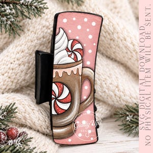 May include: A black hair claw clip featuring a pink background with white polka dots and a graphic illustration of a brown mug filled with a beverage, topped with white whipped cream and red and white peppermint candies.