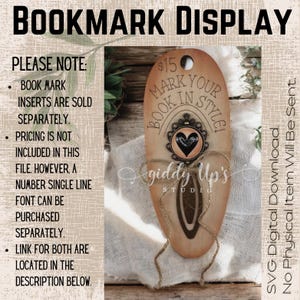 May include: A wooden bookmark display with a rustic brown finish. The display features a cutout for a bookmark and the text "Mark Your Book In Style!" with a heart-shaped embellishment. The display is tied with twine and has the text "giddy Up's Studio" below.