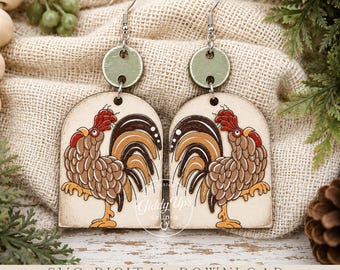 May include: A pair of dangle earrings featuring an arch-shaped wooden pendant with a brown and tan rooster illustration. Each earring has a small, round, sage green wooden topper attached to a silver-toned metal hook. The text Giddy Up Studio is visible.