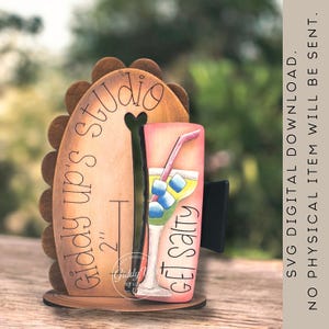 May include: Wooden desk organizer with a cutout design. The organizer features the text "Giddy up's Studio" and "Get Salty". A painted image of a cocktail glass with ice cubes and a straw is visible. The organizer is approximately 2 inches tall.