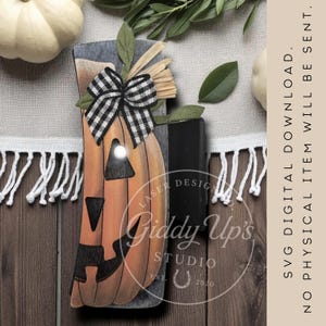 May include: A wooden pumpkin decoration with a black and white checkered bow, green leaves, and a straw accent. The pumpkin has a carved face and a light inside. The text "Giddy Up's Studio" is visible.