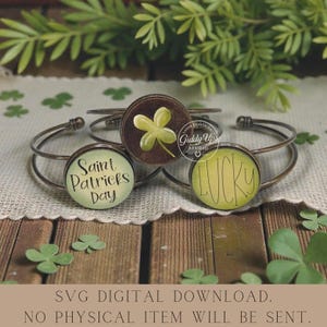 May include: Three metal bracelets with round charms. One charm says "Saint Patricks Day", another says "LUCKY", and the third has a green shamrock. The bracelets are on a wooden surface with shamrock decorations.