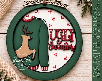 Könnte beinhalten: Ein runder Holzschmuck mit einem dunkelgrünen Rahmen und einer weißen Mitte. Er zeigt eine grüne Pullovergrafik mit einem braunen Rentier, roten Punkten und dem roten Text UGLY SWEATER. Ein schwarz-weißes Fischgrätenband ist oben befestigt.