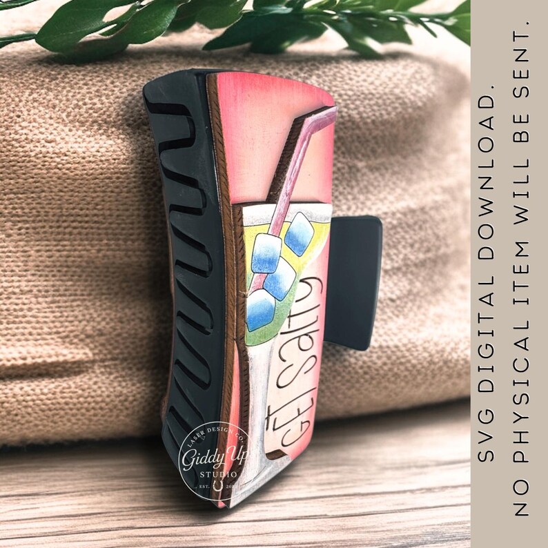 May include: A decorative hair clip featuring a colorful illustration of a refreshing drink with ice cubes and a straw. The clip has the words "Get Salty" and "SVG Digital Download" printed on it. The clip is a unique accessory.