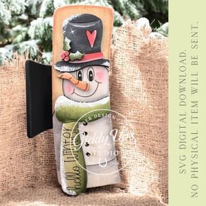 May include: A wooden snowman decoration with a black top hat, carrot nose, and green scarf. The snowman has a smiling face and the words "hello winter" are on the scarf. The decoration is attached to a black stand.