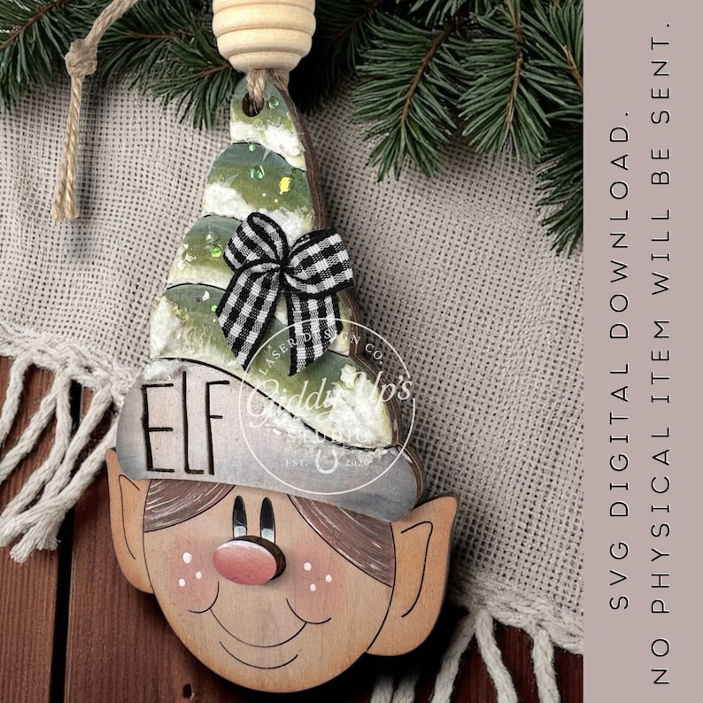 May include: Wooden elf Christmas ornament with a painted face, hat, and a green and white tree-shaped top. The ornament has a black and white checkered bow and the word "ELF" on the hat. The text "SVG DIGITAL DOWNLOAD. NO PHYSICAL ITEM WILL BE SENT." is also visible.