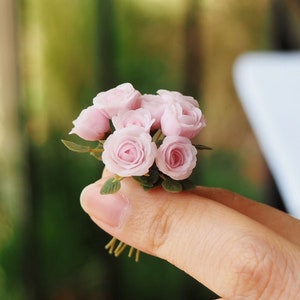 Puede incluir: Un pequeño ramo de delicadas rosas rosadas con hojas verdes, sostenido en una mano.