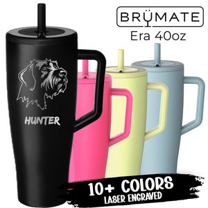 May include: A black stainless steel travel mug with a black lid and a straw. The mug has a handle and is engraved with the words "Hunter" and a graphic of a dog. The mug is shown next to three other travel mugs in pink, yellow, and blue. The text "BRÜMATE Era 40oz" and "10+ COLORS LASER ENGRAVED" is also visible.