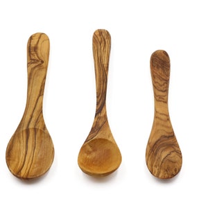 Peut inclure: Trois cuillères en bois de différentes tailles, en bois d'olivier, avec des motifs naturels de grain de bois. Les cuillères sont disposées horizontalement sur un fond blanc.