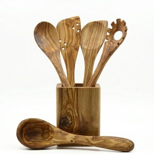 May include: A white ceramic mug with a black handle and the text "But First, Coffee" in a bold, black font. The mug is set against a blurred background, suggesting a cozy setting.