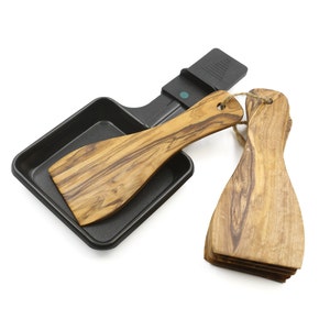 Puede incluir: Una sartén cuadrada negra con una espátula de madera y dos espátulas de madera adicionales. Las espátulas tienen un patrón de veta de madera natural.