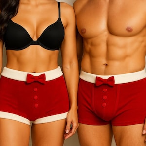 Puede incluir: Pantalones cortos tipo bóxer rojos y blancos con pajarita y detalles de botones. Los pantalones cortos se combinan con un sujetador negro. El tema general es festivo y juguetón, adecuado para una fiesta u ocasión especial.