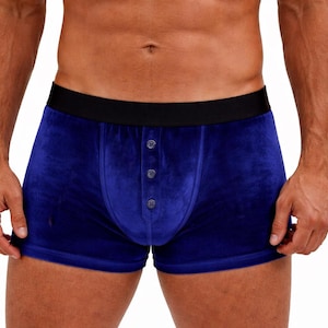 May include: Blue velvet boxer shorts with a black waistband and button closure. The underwear is a solid blue colour and has a soft, plush texture. The shorts are designed for comfort and style.