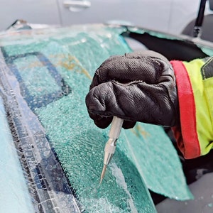 Peut inclure: Une main gantée utilise un outil pour briser une vitre de voiture. La vitre est brisée et le verre est brisé en petits morceaux.