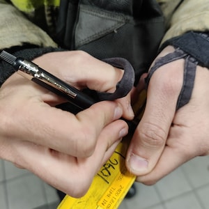 May include: A yellow card with the text "2400 LITES", "TRIPLE IN", "1993", and "D961" written on it. The card is being held by a person wearing a black leather jacket and yellow and black safety vest.