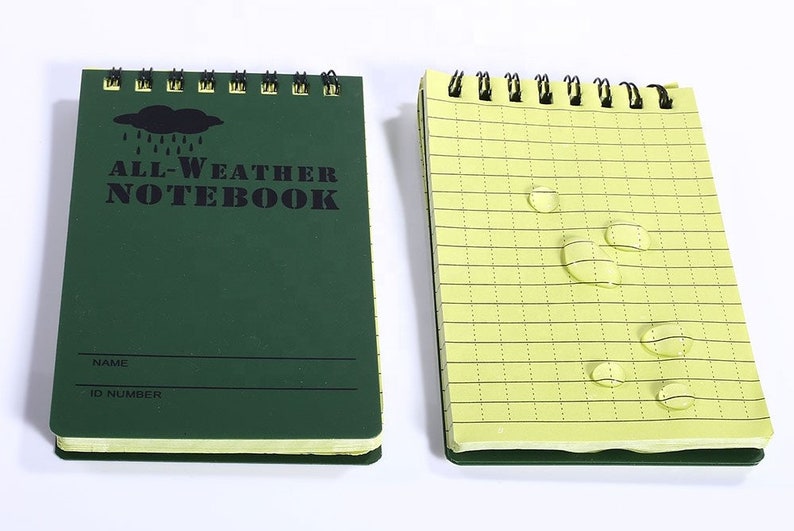 K&ouml;nnte beinhalten: Ein gr&uuml;nes Allwetter-Notizbuch mit einem schwarzen Wolken- und Regentropfen-Motiv. Das Notizbuch hat ein gelines Innenleben und ist wasserabweisend. Der Umschlag tr&auml;gt den Text "ALL-WEATHER NOTEBOOK" und Platz f&uuml;r einen Namen und eine ID-Nummer.
