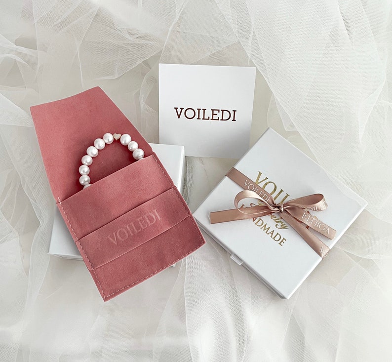 May include: A pink velvet jewelry pouch with a pearl bracelet inside. The pouch has the word "VOILEDI" embossed on it. The bracelet is in a white box with a pink ribbon and the words "VOILEDI Jewelry Handmade" on it.