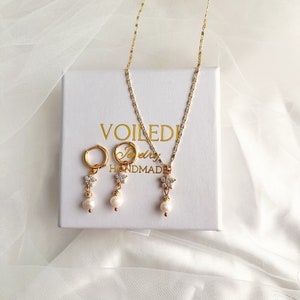 May include: A gold necklace and earrings set with a delicate flower charm and a single pearl drop. The jewelry is displayed on a white box with the text "VOILEDI Jewelry HANDMADE".