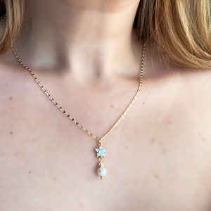 May include: A gold chain necklace with a delicate snowflake pendant and a single pearl hanging below.