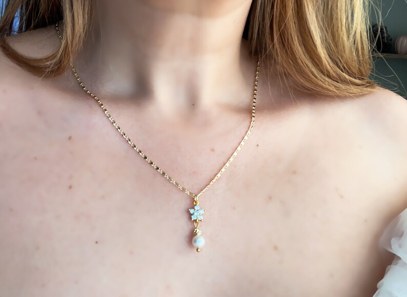 May include: A gold chain necklace with a delicate snowflake pendant and a single pearl hanging below.