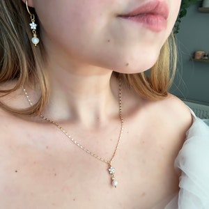 May include: A gold chain necklace with a small pearl and flower pendant. The necklace is paired with matching earrings with a pearl and flower design.