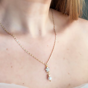 May include: A gold chain necklace with a small flower pendant and a pearl drop. The pendant is made of clear rhinestones.