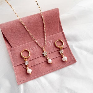 May include: A set of three gold jewelry pieces with pearl accents. The set includes a necklace and two earrings. The jewelry is displayed on a pink velvet pouch.