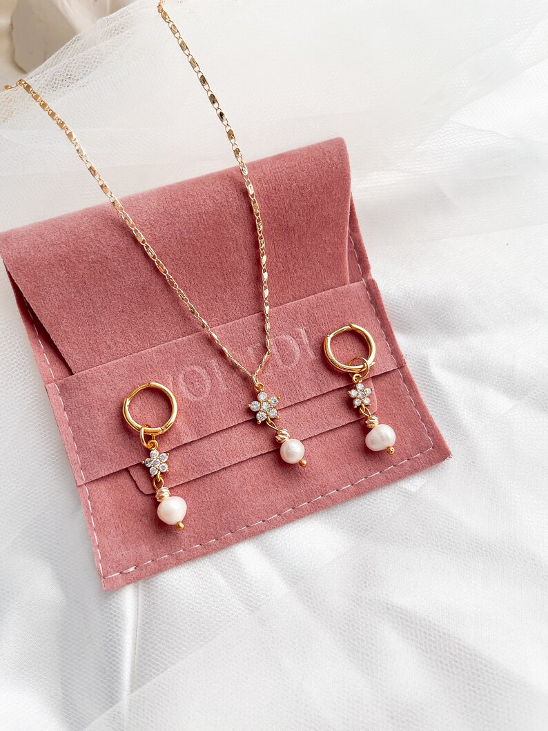 May include: A set of three gold jewelry pieces with pearl accents. The set includes a necklace and two earrings. The jewelry is displayed on a pink velvet pouch.