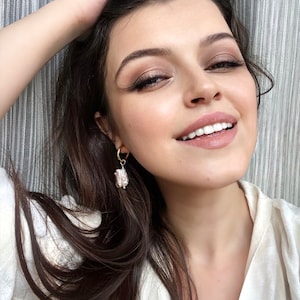 Pu&ograve; includere: Una donna con lunghi capelli scuri indossa orecchini a cerchio dorati con un ciondolo di perla. Gli orecchini pendono dalle sue orecchie.