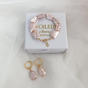 Pu&ograve; includere: Un set di gioielli in perle barocche rosa composto da un braccialetto e un paio di orecchini. Il braccialetto &egrave; realizzato con perle di forma irregolare collegate da una catena dorata. Gli orecchini sono a cerchio con una singola perla che pende da ogni cerchio. I gioielli sono presentati in una scatola bianca con il testo "VOILEDI Jewelry HANDMADE".