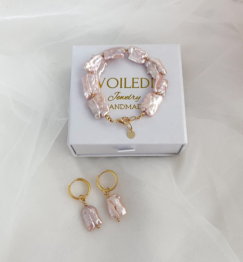Pu&ograve; includere: Un set di gioielli in perle barocche rosa composto da un braccialetto e un paio di orecchini. Il braccialetto &egrave; realizzato con perle di forma irregolare collegate da una catena dorata. Gli orecchini sono a cerchio con una singola perla che pende da ogni cerchio. I gioielli sono presentati in una scatola bianca con il testo "VOILEDI Jewelry HANDMADE".