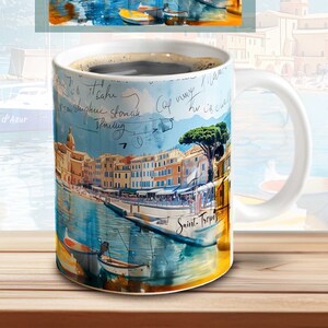 May include: White ceramic mug with a watercolor image of a harbor town with boats and buildings. The mug has handwritten text on it, including "Saint-Tropez" and "Côte d'Azur".