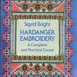 Könnte beinhalten: Ein Buch mit dem Titel Sigrid Bright Hardanger Embroidery: A Complete and Practical Course. Das Cover zeigt einen blauen Hintergrund mit einer dekorativen, bunten Hardanger-Stickerei-Borte in Pink, Grün und Orange sowie ein Dover Needlework Series Etikett.