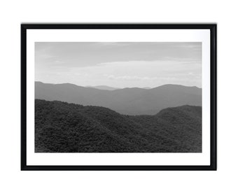 May include: A black and white photograph of a mountain range with rolling hills and a cloudy sky.