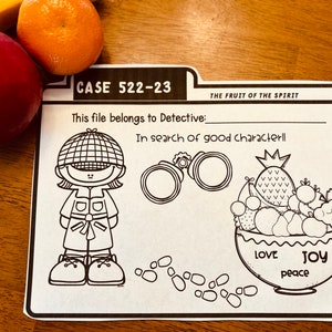 May include: Black and white printable worksheet with a detective character, magnifying glass, and a bowl of fruit. The text reads "CASE 522-23", "This file belongs to Detective:", "THE FRUIT OF THE SPIRIT", "In search of good characterll", "LOVE", "JOY", and "peace".