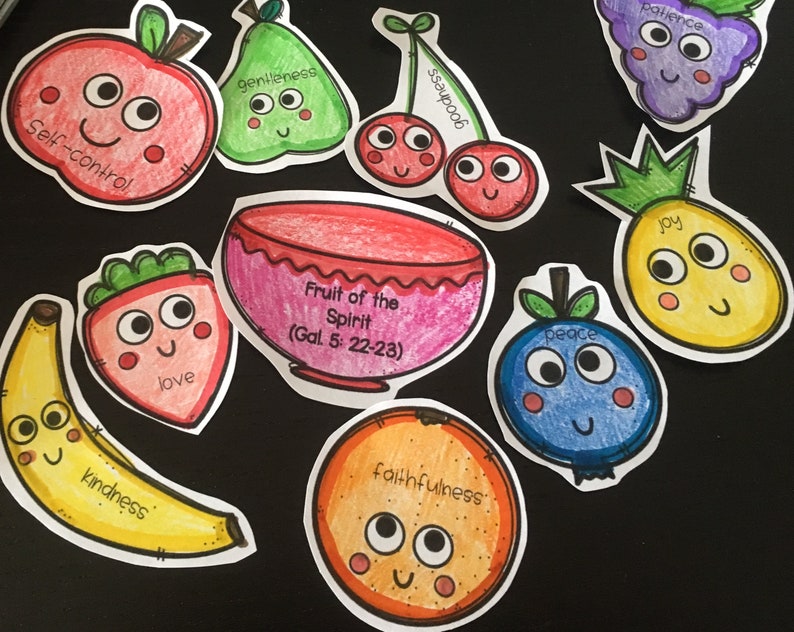 May include: A set of colorful fruit-shaped paper cutouts with faces and words like "love", "joy", "peace", and "kindness". The cutouts are arranged on a black background. The text "Fruit of the Spirit (Gal. 5: 22-23)" is written on a pink bowl cutout.