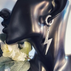 May include: Silver lightning bolt dangle earring with a silver hoop. The earring is on a black mannequin head.