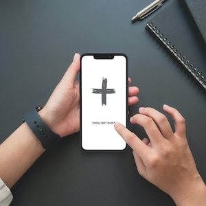 May include: A black smartphone with a white screen displaying a black plus sign and the text "THOU ART DUST".