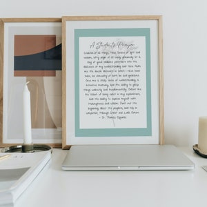 Peut inclure: Impression encadrée avec le texte "A Student's Prayer" en écriture élégante. L'impression a un fond bleu clair et est dans un cadre en bois. Un ordinateur portable, une bougie et d'autres œuvres d'art encadrées sont en arrière-plan.