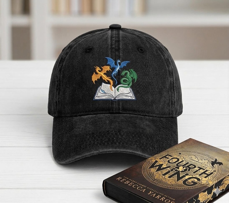 May include: Black denim baseball cap featuring an embroidered design of three dragons in orange, blue, and green above an open book. The cap is a classic six-panel design with a curved brim.
