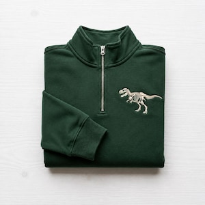 Op de afbeelding: Donkergroen sweatshirt met een kwartrits, zilveren rits en een dinosaurus skelet geborduurd op de borst. Het sweatshirt is opgevouwen, met geribde manchetten en kraag.