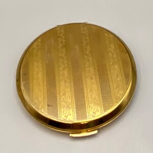 May include: A gold-toned compact mirror with a striped and floral pattern.