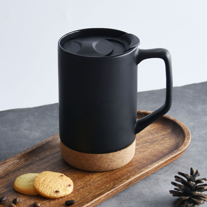 May include: A black ceramic mug with a cork bottom and a lid. The mug is sitting on a wooden tray with two cookies.