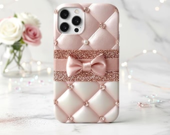May include: Pink and white quilted phone case with a bow and glitter accents. The case features a bow in the center, with a glitter band above and below it. Rhinestones are placed at the intersections of the quilted pattern.